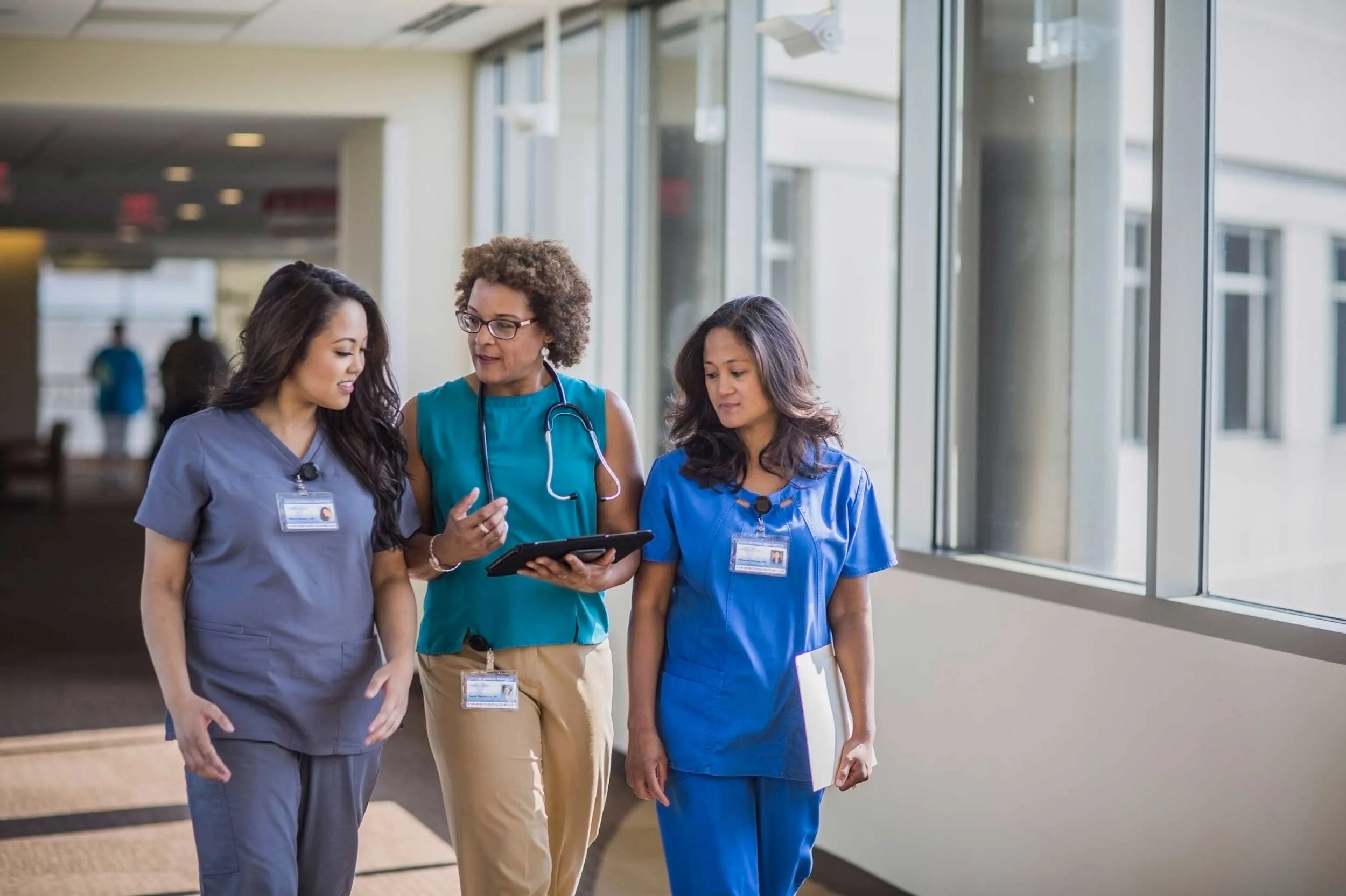 Three healthcare workers walking down the hallway looking at a tablet device while talking